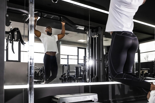 Hombre africano en forma y musculoso tirando hacia arriba en la barra horizontal en un gimnasio