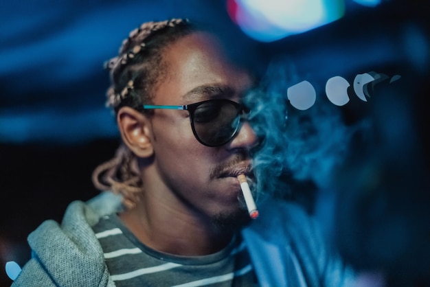 Hombre africano fumando un cigarro, en las luces de la ciudad de fondo. foto de alta calidad