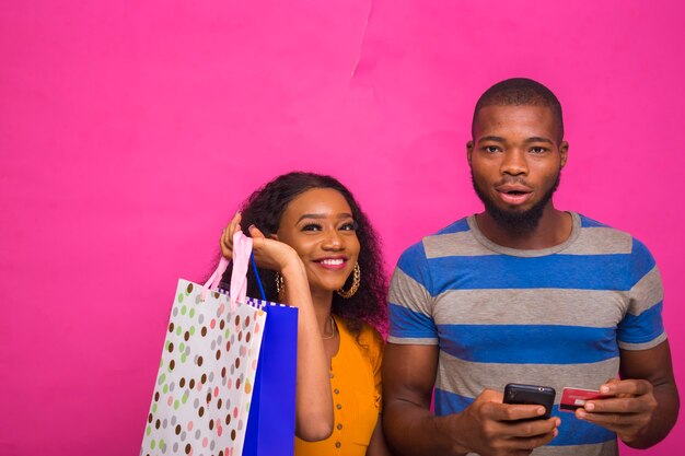 Hombre africano guapo de compras en línea para su amigo mientras sostiene bolsas de compras en su mano.
