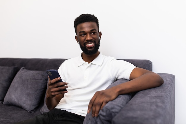 Hombre africano guapo haciendo una llamada telefónica a través de airpods mientras está sentado en un sofá en su sala de estar