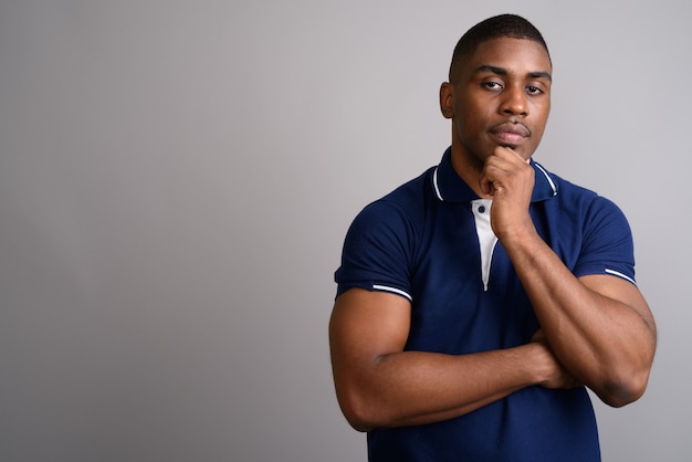 Hombre africano guapo joven con camisa polo azul sobre gris