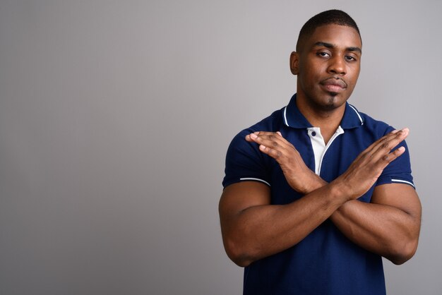 Hombre africano guapo joven con camisa polo azul sobre gris