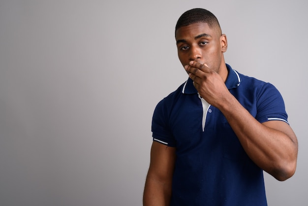 Hombre africano guapo joven con camisa polo azul sobre gris