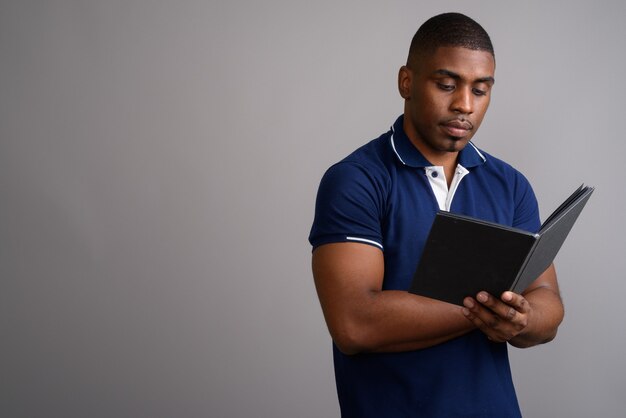 Hombre africano guapo joven con camisa polo azul sobre gris