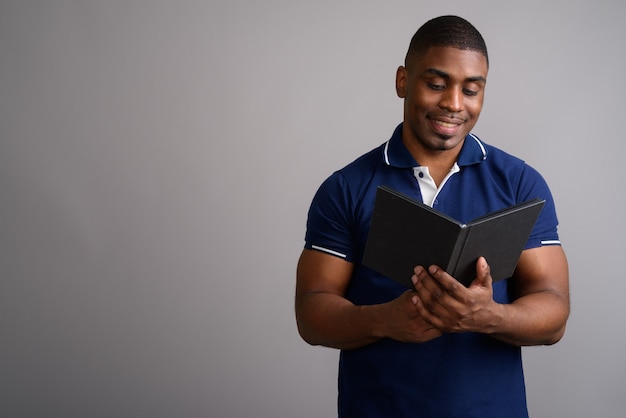 Hombre africano guapo joven con camisa polo azul sobre gris