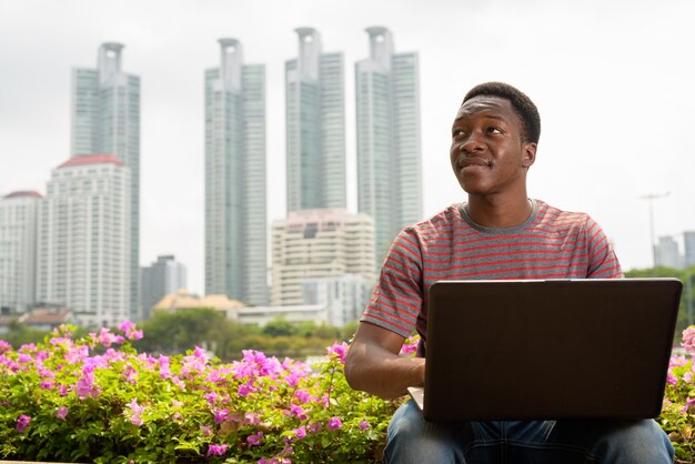 Hombre africano guapo joven con ordenador portátil en el parque