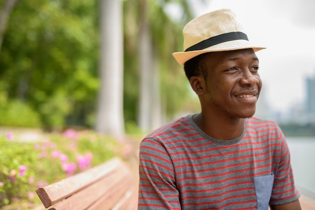 Hombre africano guapo joven sonriendo y pensando en el parque