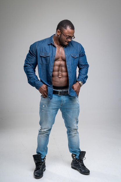 Hombre africano guapo con el torso desnudo con camisa de jeans Hombre atlético en lijado de mezclilla sobre fondo blanco Modelo masculino culturista con gafas