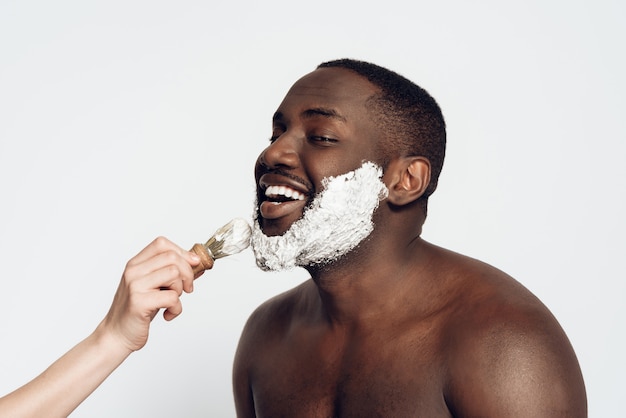 El hombre africano mancha la crema de afeitar en cara afeitando la brocha.