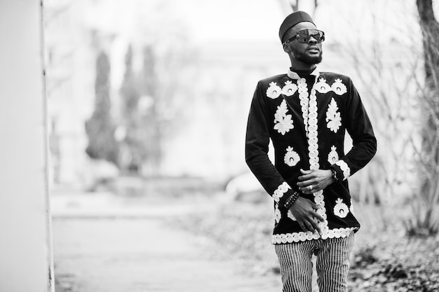 Hombre africano mega elegante en pose de chaqueta tradicional Chico negro de moda con sombrero y gafas de sol