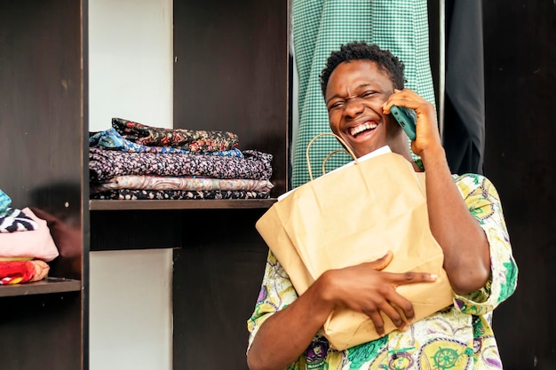 Foto hombre africano multitarea con un teléfono celular y una bolsa de compras abrazando la tecnología minorista moderna