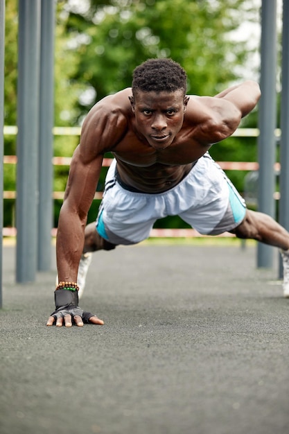 Hombre africano musculoso haciendo flexiones contra el cielo azul Fuerte atleta masculino haciendo ejercicio al aire libre