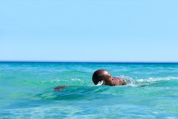 Hombre africano nadando en el agua del océano