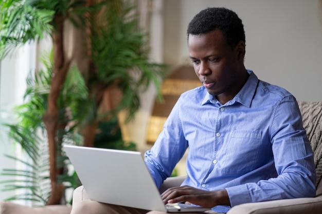 Hombre africano navegando por Internet en su habitación en casa Trabajando desde casa en cuarentena Concepto de distanciamiento social Orientación vertical