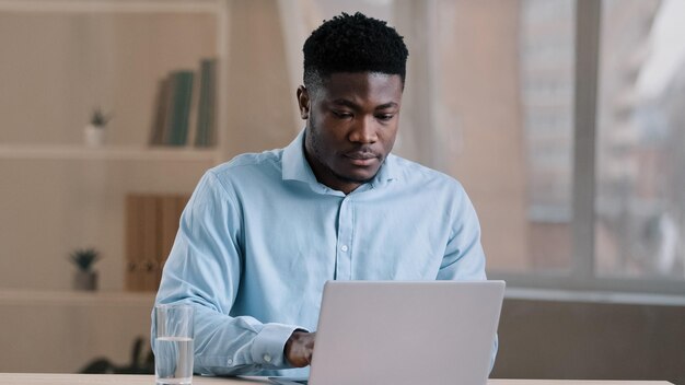 Hombre africano ocupado y estudiante sentado en la oficina de casa escribiendo en la computadora portátil