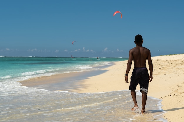 Un hombre africano en una playa tropical camina por la orilla