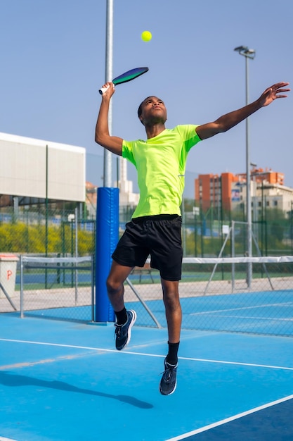 Hombre africano saltando para golpear la pelota jugando pickleball al aire libre