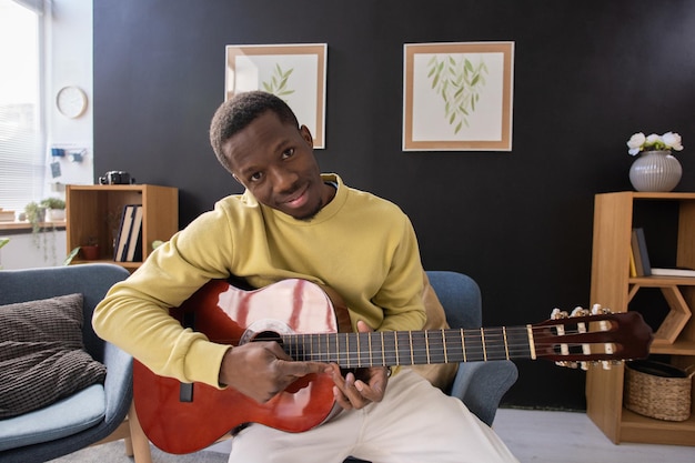 Hombre africano sonriente joven con guitarra acústica sentado frente a cámara