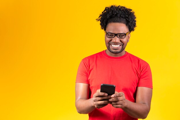 Hombre afro con anteojos sobre fondo amarillo sonriendo usando celular