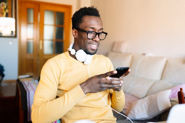 Hombre afro en casa con teléfono inteligente y computadora portátil