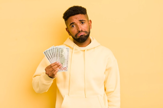 Hombre afro cool que se siente triste y quejumbroso con una mirada infeliz y un concepto de billete de dólar llorando