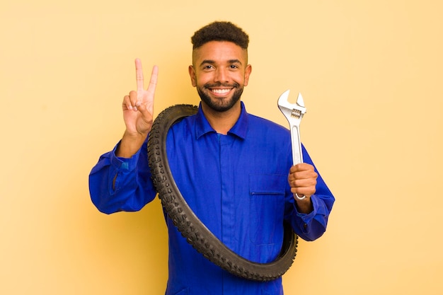 Hombre afro cool sonriendo y luciendo feliz gesticulando victoria o concepto de reparador de bicicletas de paz