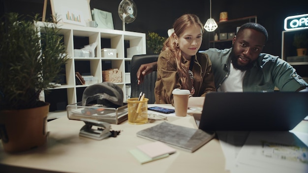 Foto hombre afro coqueteando abrazando a una bella dama cerca de una laptop en una oficina hipster