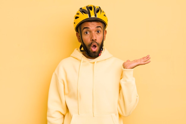 Hombre afro negro que parece sorprendido y conmocionado con la mandíbula caída sosteniendo un concepto de bicicleta de objeto