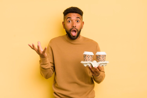 Hombre afro negro que se siente extremadamente conmocionado y sorprendido para llevar el concepto de café