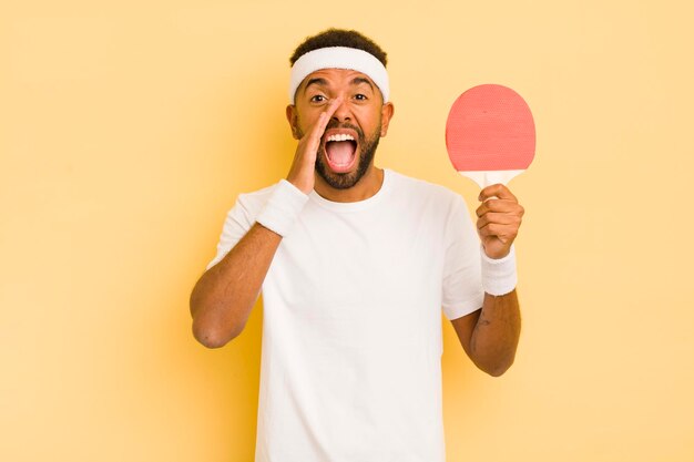 Hombre afro negro que se siente feliz dando un gran grito con las manos al lado del concepto de ping pong en la boca