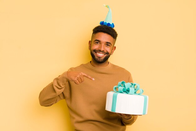 Hombre afro negro sonriendo alegremente sintiéndose feliz y señalando el concepto de cumpleaños lateral