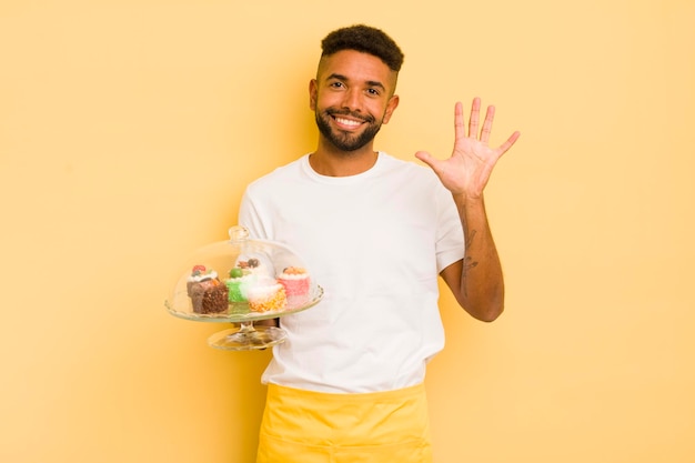 Hombre afro negro sonriendo y luciendo amigable mostrando el concepto de pasteles caseros número cinco