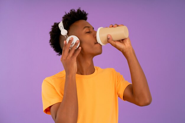 Hombre afro tomando café mientras escucha música con auriculares.