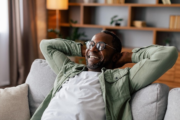 Hombre afroamericano adulto satisfecho con gafas y descanso informal y relajación, disfrute de la comodidad, la paz y el tiempo libre