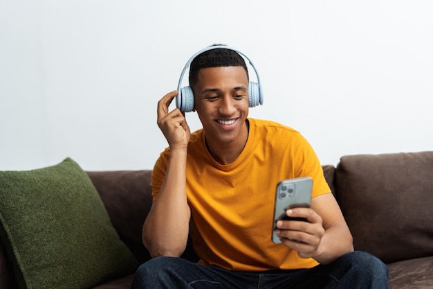 Hombre afroamericano atractivo sonriente escuchando música con auriculares sosteniendo un teléfono móvil