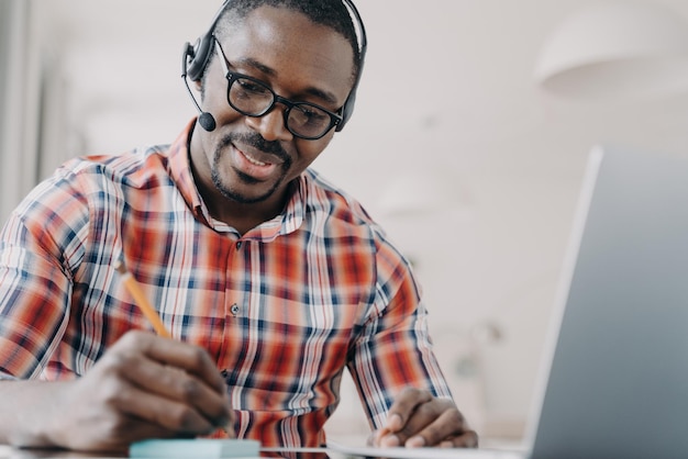 Hombre afroamericano en auriculares tiene chat de video en la computadora portátil Lección remota Servicio de atención al cliente