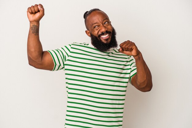 Hombre afroamericano con barba aislado sobre fondo rosa celebrando un día especial, salta y levanta los brazos con energía.