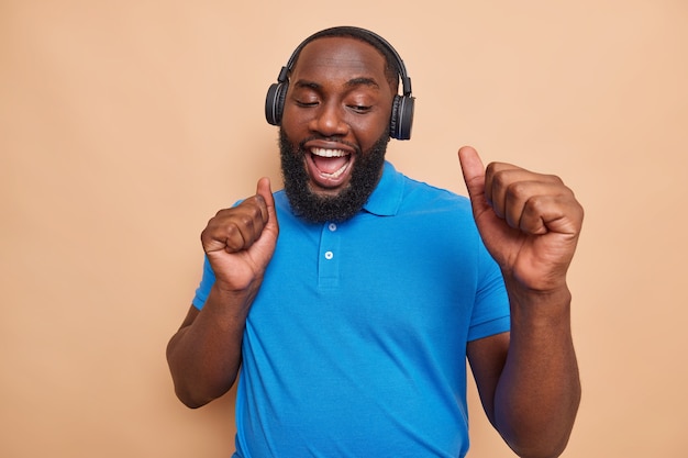 Hombre afroamericano barbudo alegre alegre baila con el ritmo de la música hace golpe de puño