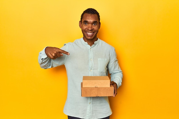 Hombre afroamericano con cajas de comida persona de estudio amarilla señalando con la mano
