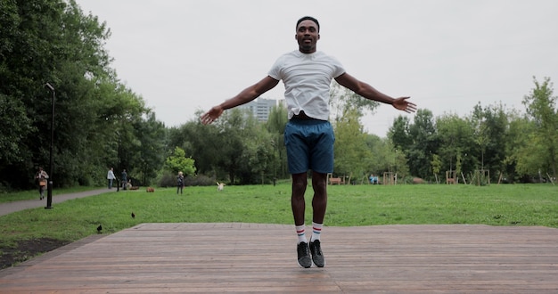 Hombre afroamericano calentando con ejercicios antes de un entrenamiento intenso al aire libre. Calentamiento de los músculos antes de trotar. Deportes al aire libre.