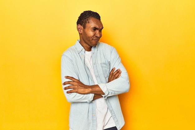 Hombre afroamericano en camisa azul estudio amarillo sospechoso incierto examinándote