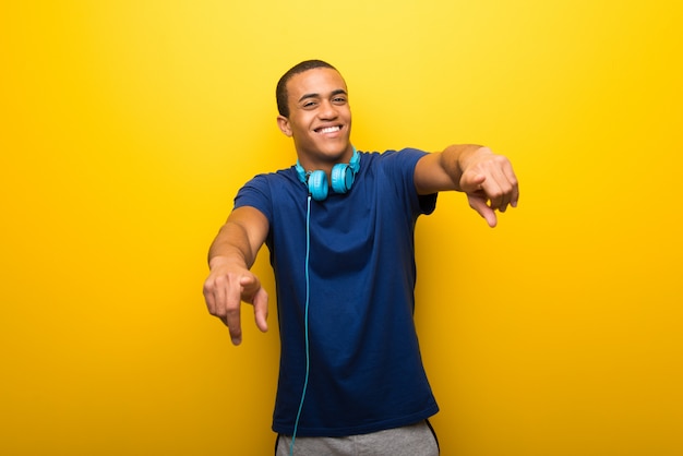 Hombre afroamericano con camiseta azul sobre fondo amarillo que señala con el dedo mientras sonríes