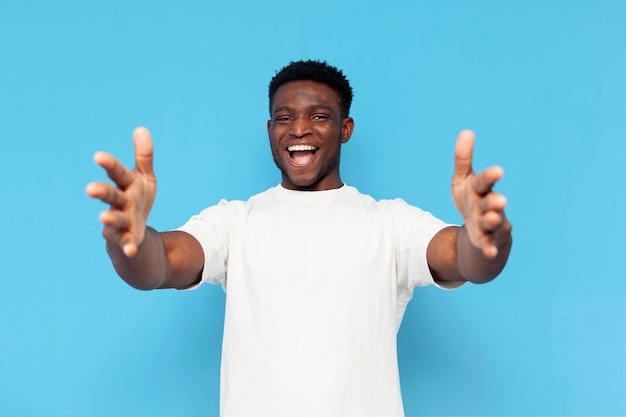 hombre afroamericano en camiseta blanca extiende los brazos hacia adelante y muestra un abrazo