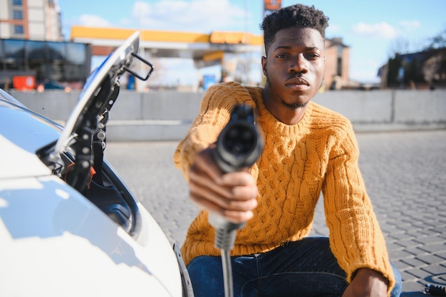 Hombre afroamericano cargando su coche eléctrico.