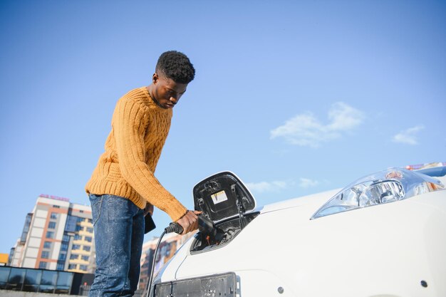 Hombre afroamericano cargando su coche eléctrico.