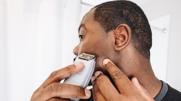 Hombre afroamericano en casa en el baño cortando el pelo con tijeras