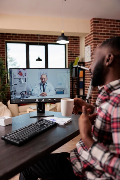 Hombre afroamericano charlando con un médico en una videoconferencia de telemedicina, usando una videoconferencia de telesalud en línea para hablar con un médico sobre la atención médica. Uso de computadora con cámara web de forma remota.