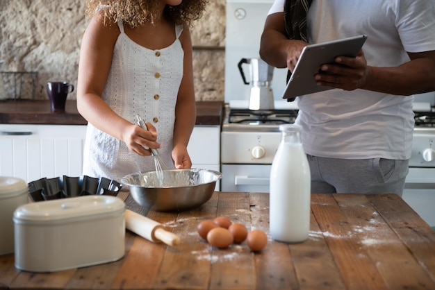 Hombre afroamericano cocinando con su hija mientras mira la receta en línea en su tableta