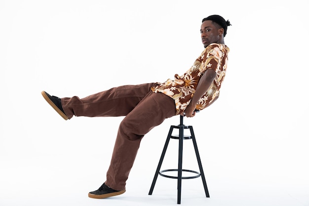 Foto hombre afroamericano divertido posando en silla sobre fondo blanco en estudio aislado mirando a la cámara