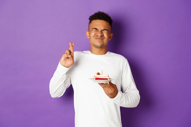 Hombre afroamericano emocionado celebrando un cumpleaños, pidiendo deseos, sosteniendo el pastel de cumpleaños